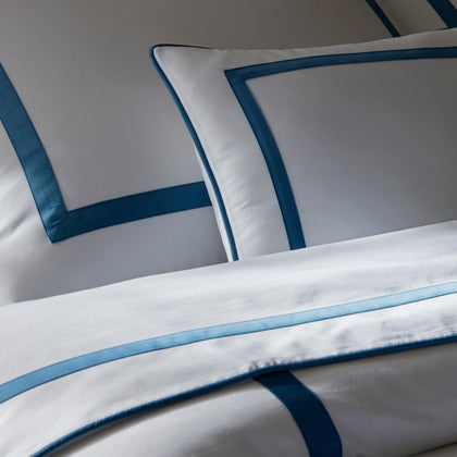 Close-up of white Louise bedding with blue ribbon trim in two shades, with a matching pillow.