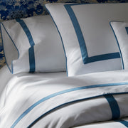 Close-up of white Louise bedding with blue ribbon trim, against a blue-and-white patterned headboard.