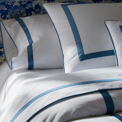 Close-up of white Louise bedding with blue ribbon trim, against a blue-and-white patterned headboard.