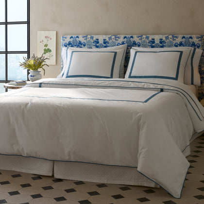 White Louise bedding with blue bordered trim, styled on a bed with a floral headboard.