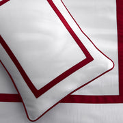 Close-up of a white pillow sham and bedding with a red pique border.