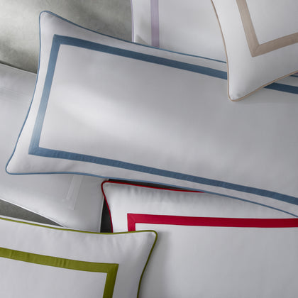White pillow shams with pique borders in slate blue, red, olive, and tan, overlapping on a bed.