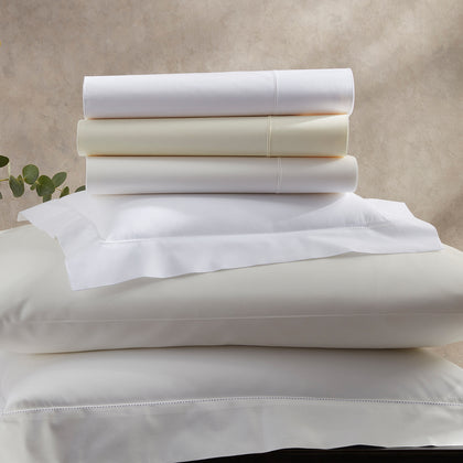 White and ivory Luca Hemstitch sheets stacked with hemstitch trim, beside a eucalyptus sprig.