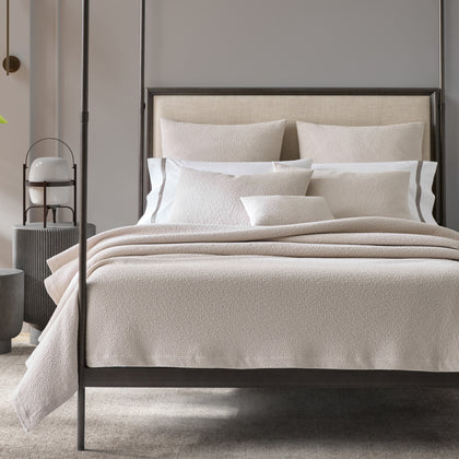 Ivory Malibu textured bouclé bedding styled on a bed with a dark four-poster frame.