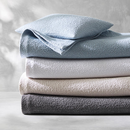 Malibu textured bouclé bedding stacked in blue, gray, tan, and charcoal.