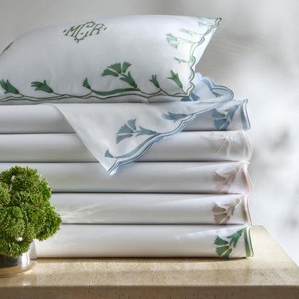 White Marcella sheets with vine-embroidered scalloped trim in assorted colors, stacked with a monogrammed pillow.
