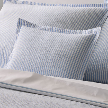 Close-up of pale blue-striped Matteo pillows, with white sheets trimmed in blue.