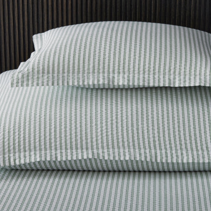 Close-up of sage green-striped Matteo pillow and sheets against a dark slatted wood headboard.