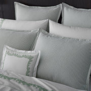 Close-up of sage green-striped Matteo pillows and white sheets embroidered with a green vine motif.