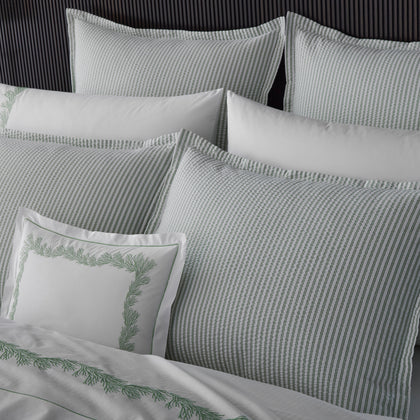 Close-up of sage green-striped Matteo pillows and white sheets embroidered with a green vine motif.
