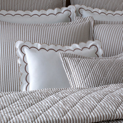 Close-up of taupe-striped Matteo pillows with white scalloped-trim pillows, on quilted bedding.