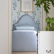Pale blue-striped Matteo bedding on an upholstered headboard and bed, in an alcove with floral wallpaper and green ceramic lamps.