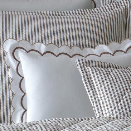 Close-up of taupe-striped Matteo pillows with a white scalloped-trim pillow, on quilted bedding.
