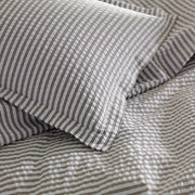 Close-up of taupe-striped Matteo seersucker pillow and sheets on a bed.