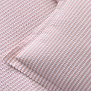Close-up of pink-striped Matteo seersucker sheets and pillow, folded on a bed.