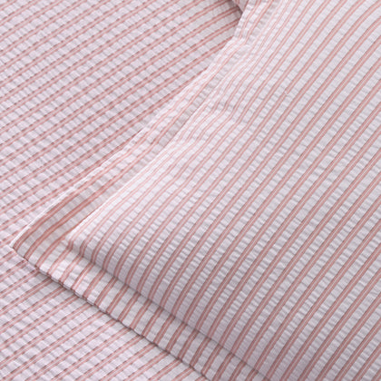 Close-up of pink-striped Matteo seersucker sheets and pillow, folded on a bed.