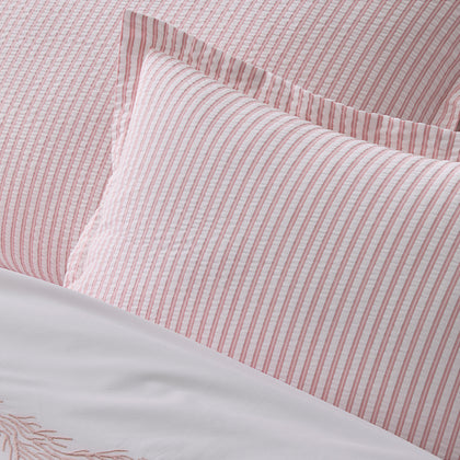 Close-up of pink-striped Matteo pillows, with white sheets embroidered with a pink floral motif.