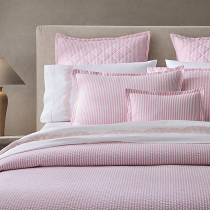 Pink-striped Matteo bedding with a white embroidered sheet, styled on a bed with an upholstered headboard.