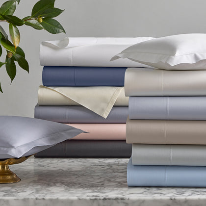 Milano Hemstitch sheets stacked in an array of solid colors, on a marble table.