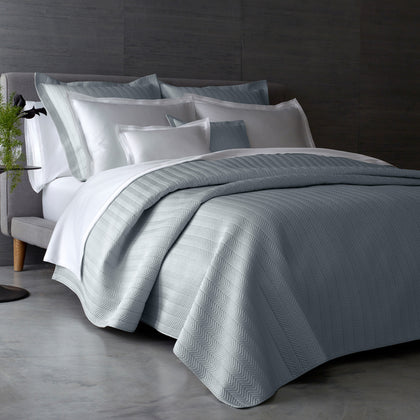 Gray Netto chevron-textured quilted bedding styled on a bed with white sheets.