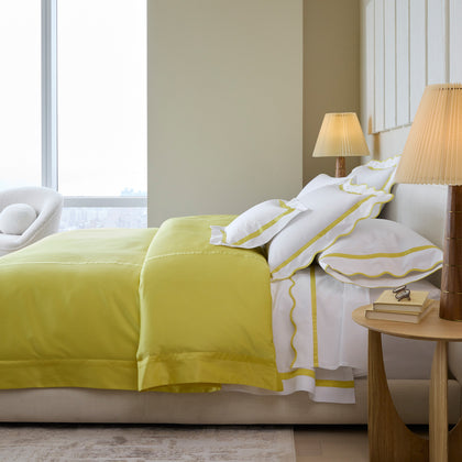 Lemon yellow Nocturne sateen bedding with white scalloped shams in a bedroom