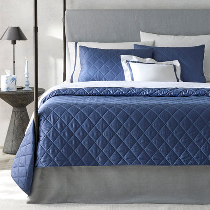 Navy Nocturne diamond-quilted bedding styled on a bed with a gray upholstered headboard.