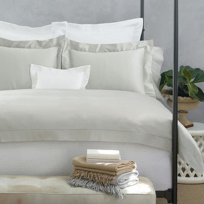 Taupe Nocturne Hemstitch bedding styled on a bed with fringed throws folded on a bench.