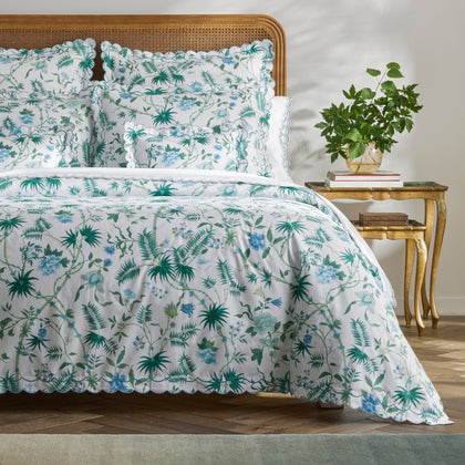 Green and blue Palmyra botanical print bedding styled on a bed with a rattan headboard.