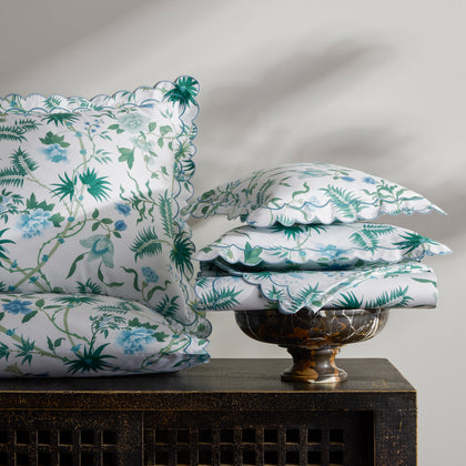 Green and blue Palmyra botanical print pillows and sheets, stacked on a dark carved cabinet.