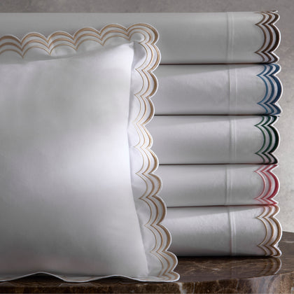 White Stella sheets with double-scalloped embroidered trim in assorted colors, stacked on a marble table.