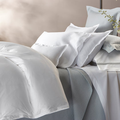 White Talita Satin Stitch bedding with blue quilted shams, styled on a bed.