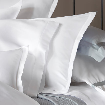 White Talita Satin Stitch bedding styled on a bed with a gray quilted throw.
