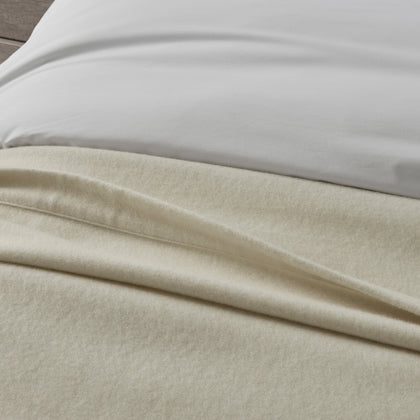 Close-up of ivory Venus blanket texture draped on a bed.