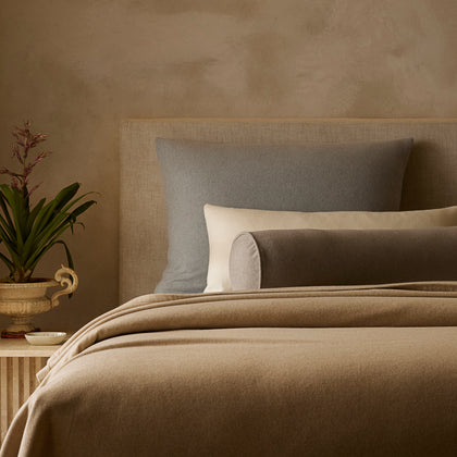 Tan Venus cashmere blanket draped on a bed with a gray pillow and bolster.