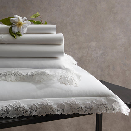 White Virginia sheets with floral lace trim, stacked on a black table beside a white flower.