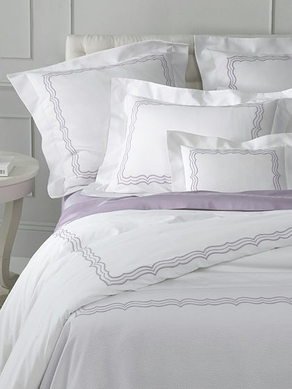 White bedding set with lavender purple accents and gray wavy embroidered borders, styled on a bed with matching pillows.