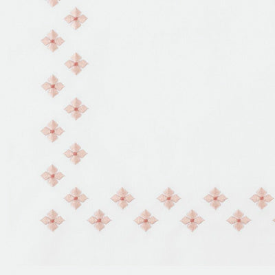 Close up of a napkin with a delicate border of small pale pink embroidered floral motifs along the left and bottom edges.