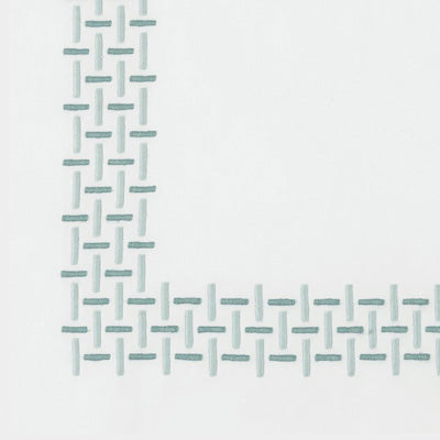 Close up of a napkin with a repeating stitched geometric pattern in a muted light blue-green along the left and bottom edges.