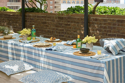 Apollo Stripe blue and white tablecloth and napkins on a rooftop dining table with woven chargers and yellow roses