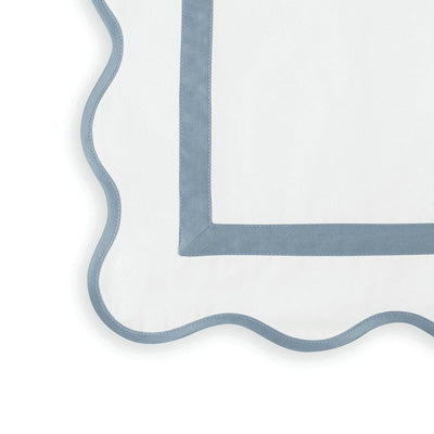 Close up of a napkin featuring a dusty blue scalloped border.