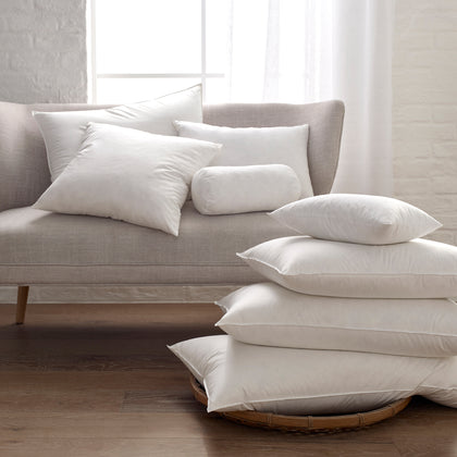 Montreux three-chamber down pillows stacked on a sofa and floor.