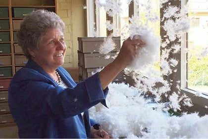 Woman sorting a handful of white down clusters at a processing facility.