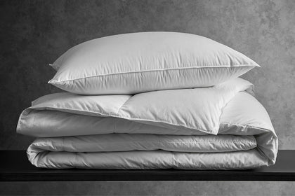 Chalet down pillow stacked on a folded comforter on a wooden bench.