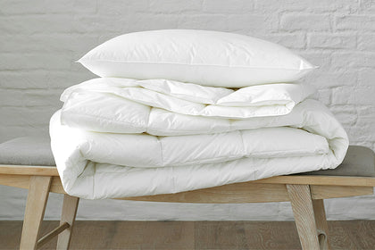 Libero hypoallergenic pillow stacked on a folded comforter on a bench.