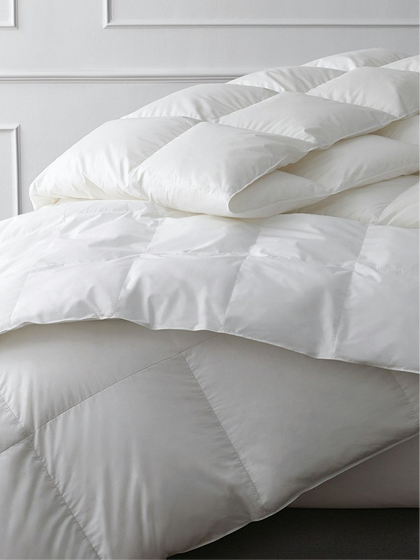 White quilted down comforter draped over the edge of a bed.