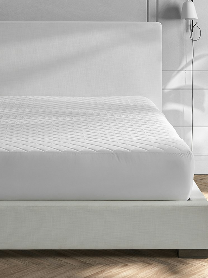 Quilted white mattress pad fitted on a bed frame.