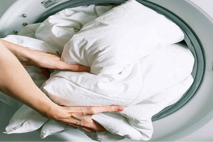 Hands loading a white down comforter into a washing machine.