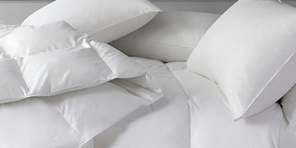 Stack of white down pillows and a comforter on a bed.