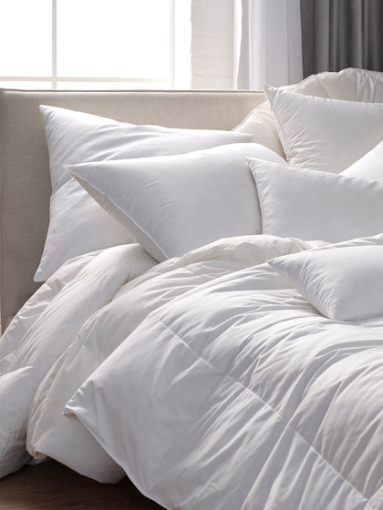 Down collection comforter and pillows, fluffy and white, piled on a bed by a window