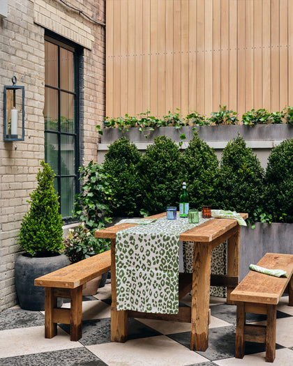 Outdoor patio dining table at House of Matouk styled with a leopard-print runner and topiary